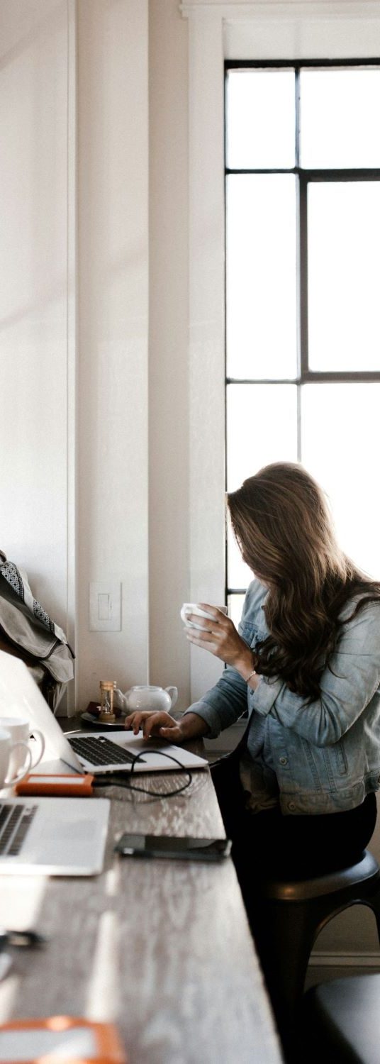 Professional English for business – clear communication across cultures. Woman working on a laptop in a bright office with coffee — representing professional English communication and international business.
