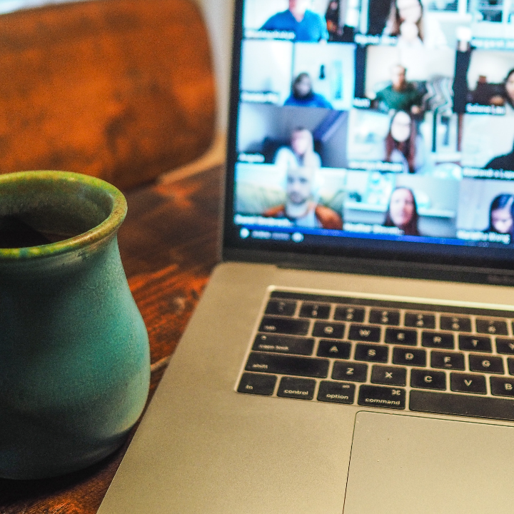 A green coffee cup on a table located next to a laptop showing the participants of a live English class.